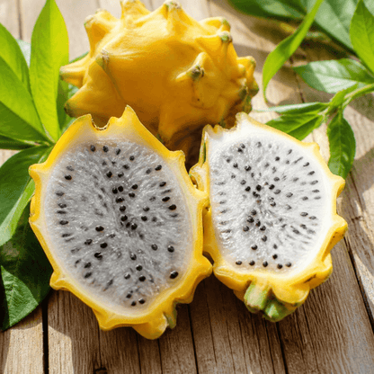 Yellow dragon fruit with one whole fruit and two halves cut open, showing white flesh with black seeds, arranged on a wooden surface with green leaves.